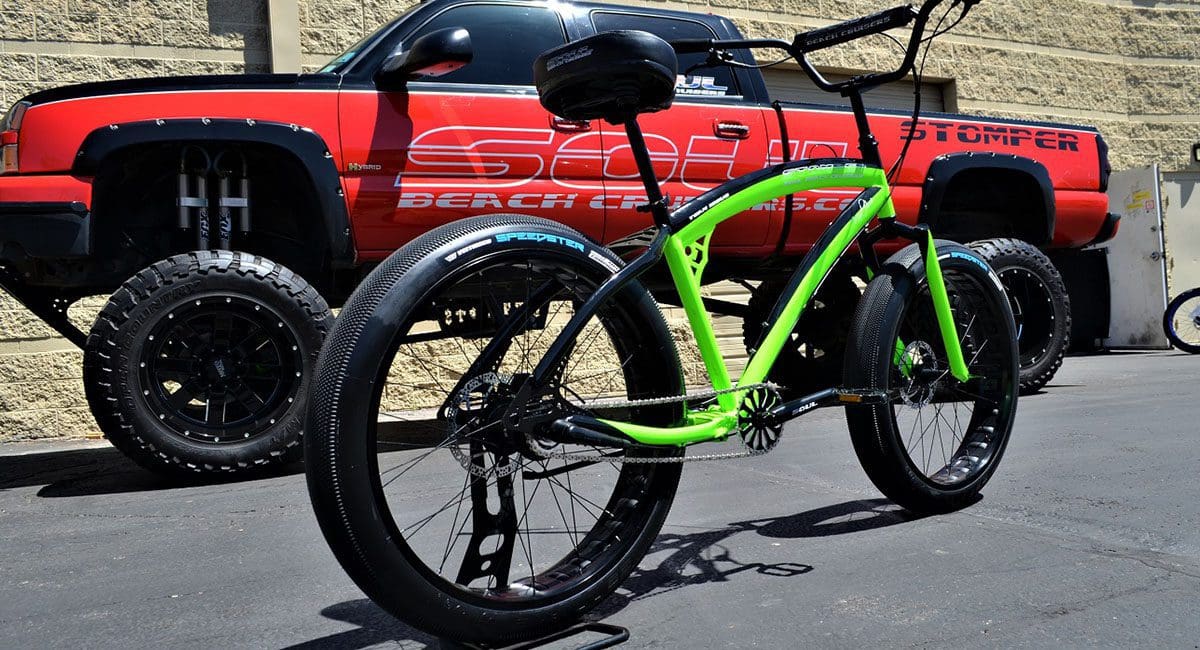 A green Pedal Stomper bike parked in front of a truck.