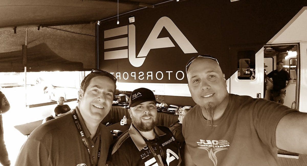 Three men posing for a photo in front of a tent featuring SOULFAST EBIKES.