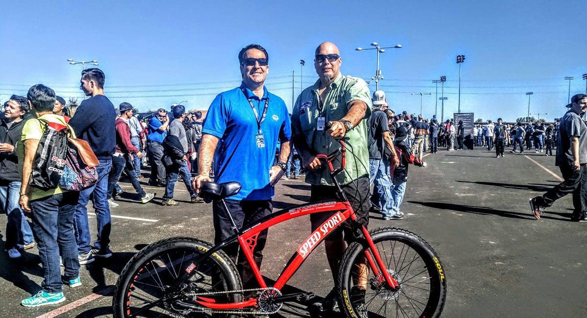Two men standing next to a red FAST EBIKE in a crowd.