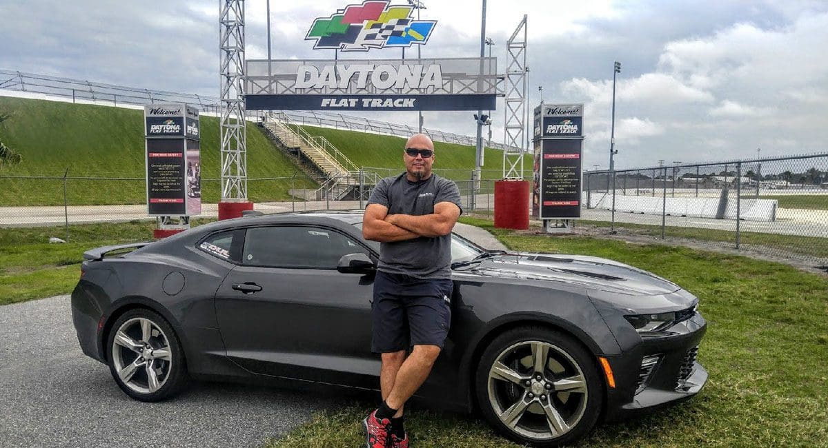 A man standing next to a black chevrolet camaro from SOULFAST EBIKES.