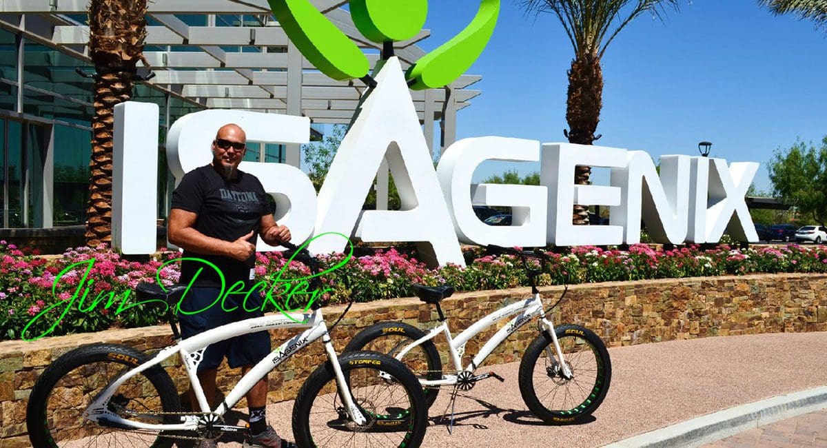 A man standing next to a bicycle in front of the isagenix sign.