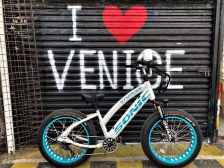 A MISS SABER PRO WHITE & TEAL 24" bike parked in front of a garage with the words i love venice written on it.