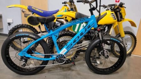 Blue bicycle and two yellow motorbikes indoors.