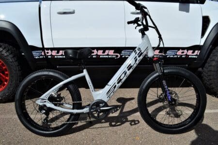 A white electric bike parked in front of a truck.