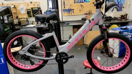 A pink and grey bike is on display in front of a wall.