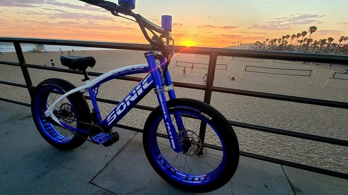 A blue and white SOULFAST e-bike sits on a railing near the beach in Clearwater, FL.