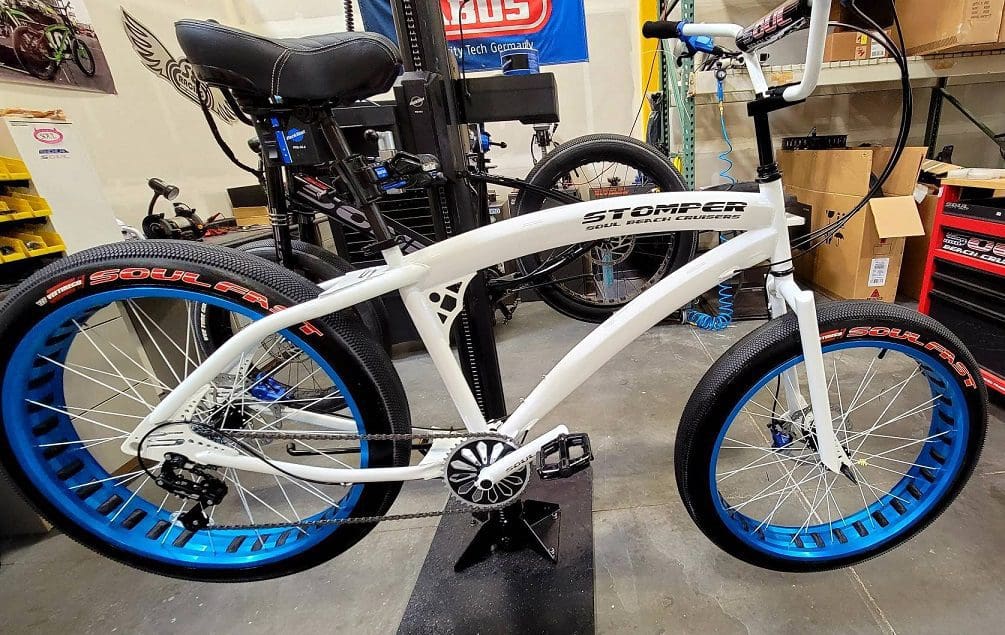 A white bicycle with blue wheels sitting on top of a stand.
