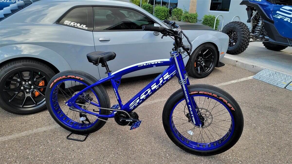 A blue bicycle parked in front of a car.
