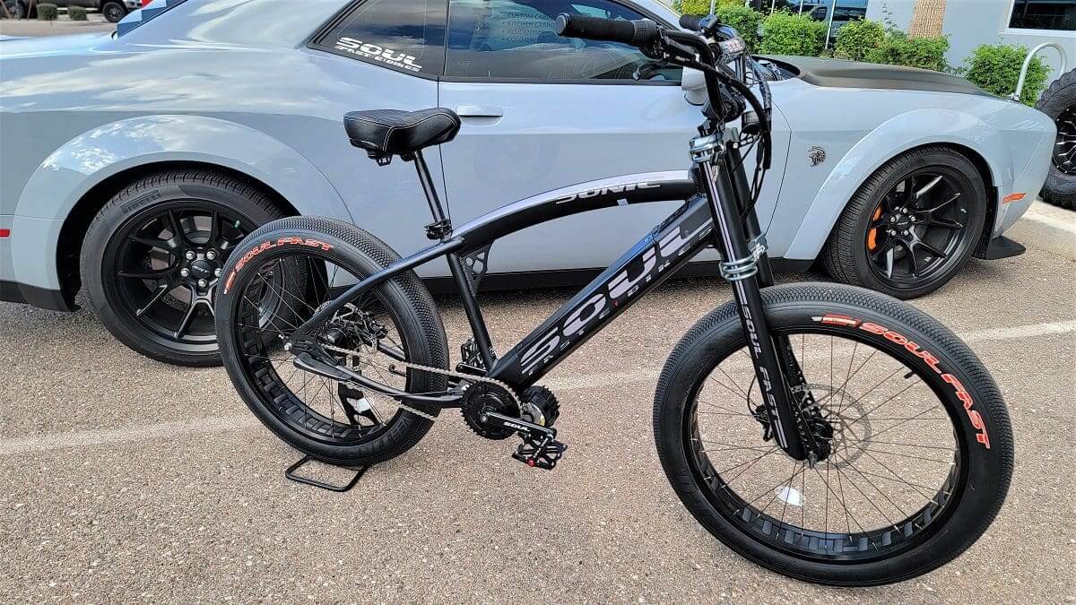 A black bicycle parked in front of a white car.