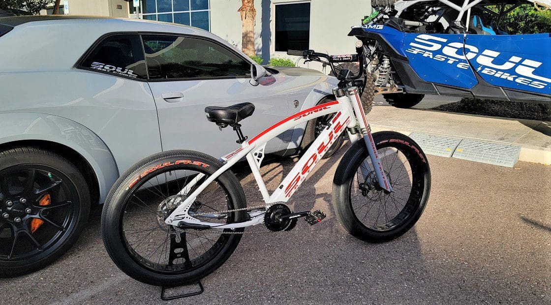 A white and red bicycle parked in front of two cars.