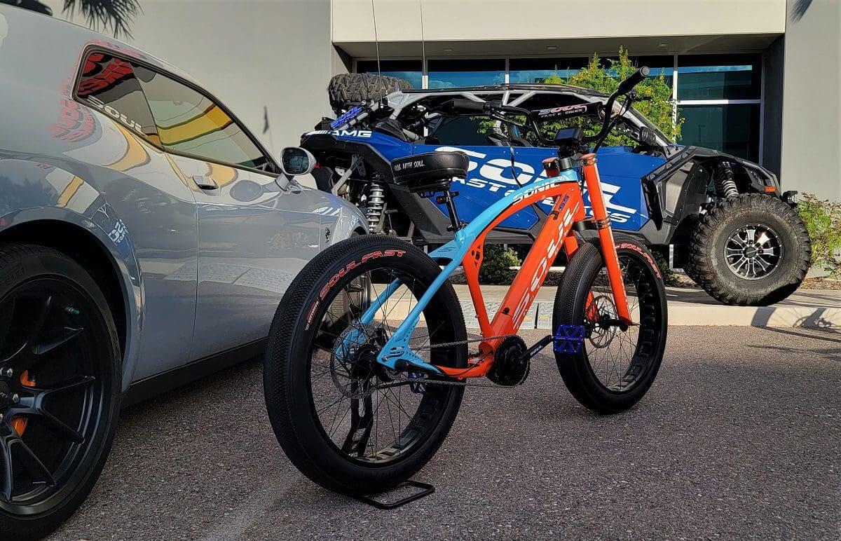 A blue and orange bike parked in front of a car.