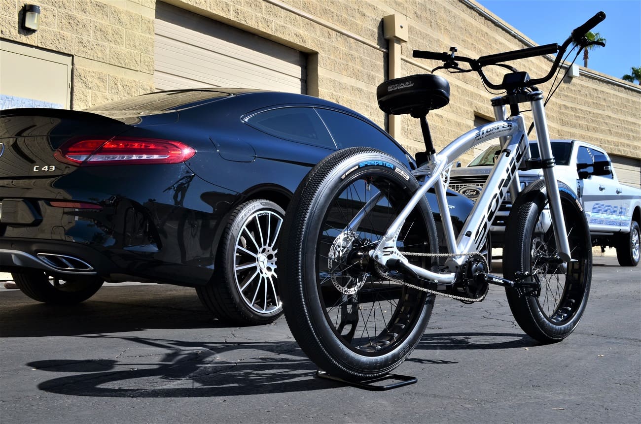 White bicycle parked beside a black car.