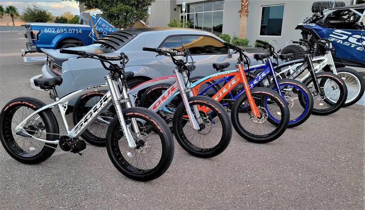 Five colorful bikes parked beside a car.