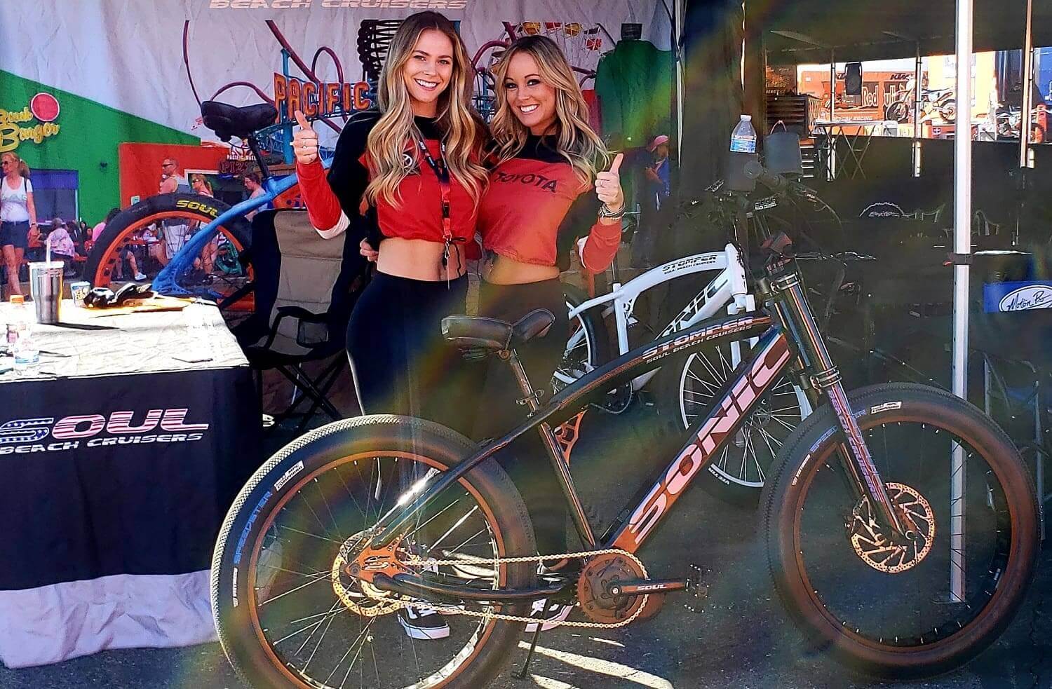 Two women posing with a black bicycle.