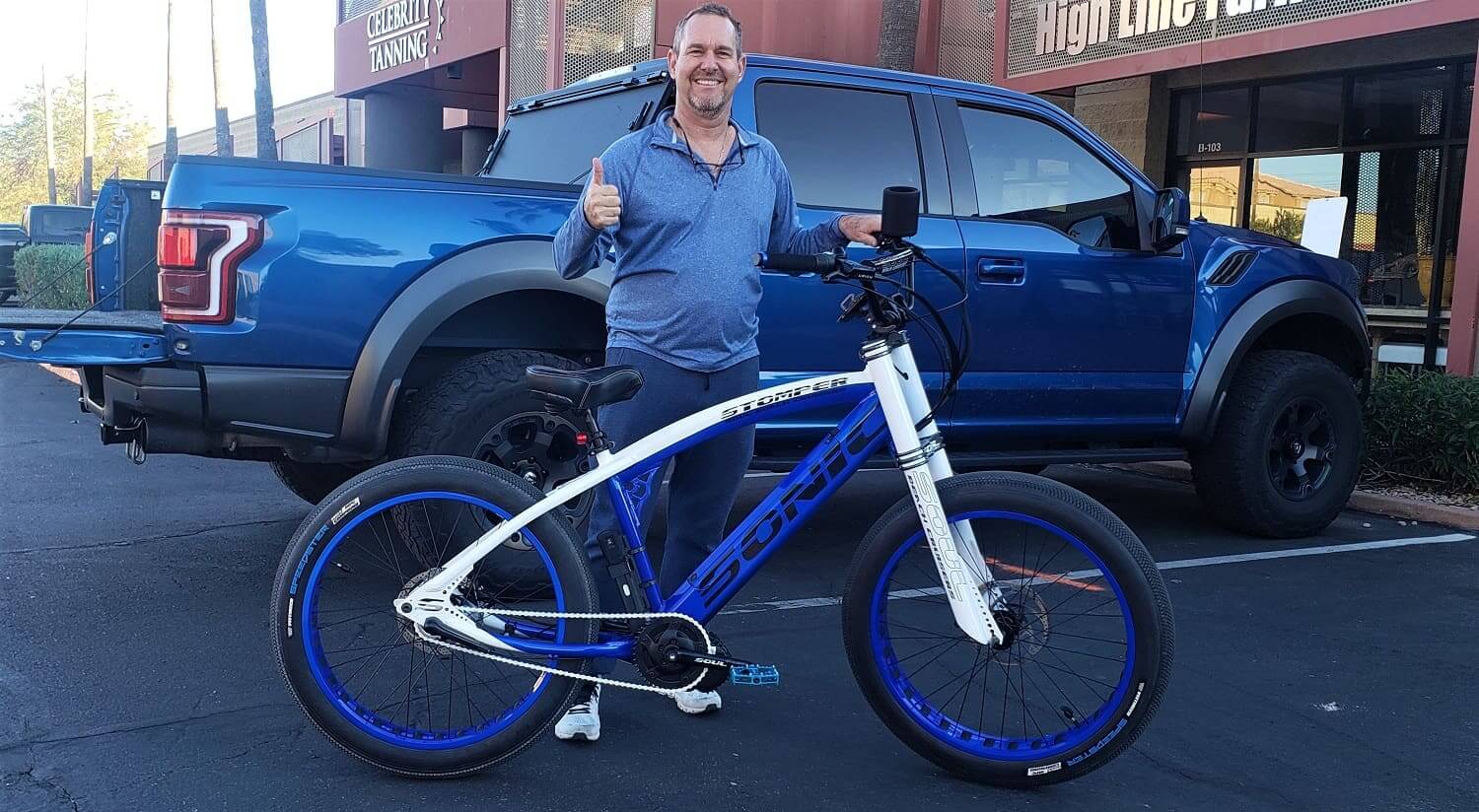 Man with blue bike and truck smiling.