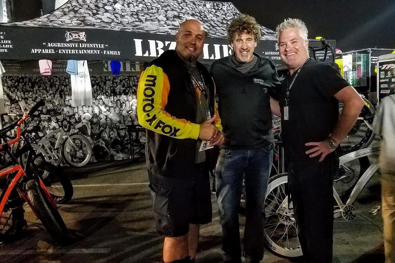 Three men smiling and posing together at a SOULFAST EBIKES motorcycling event at night.