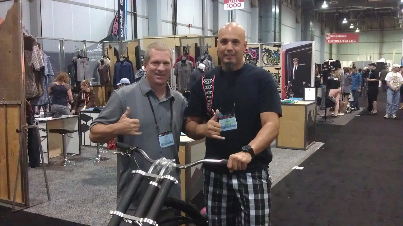 Two men posing with thumbs up beside a SOULFAST EBIKE at an indoor event.