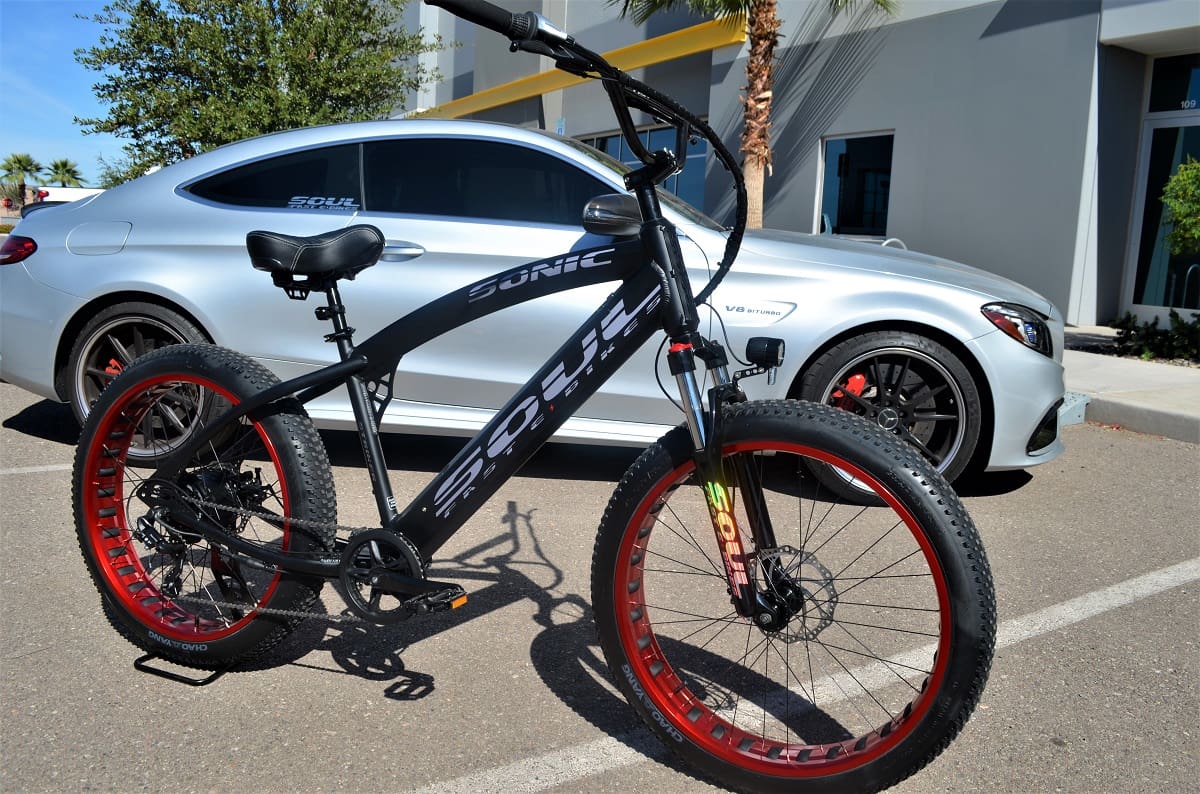 Matte-black e-bike leaning near silver sports coupe