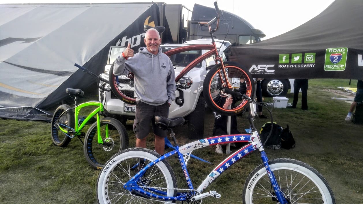 Man showcasing colorful bicycles at outdoor event.