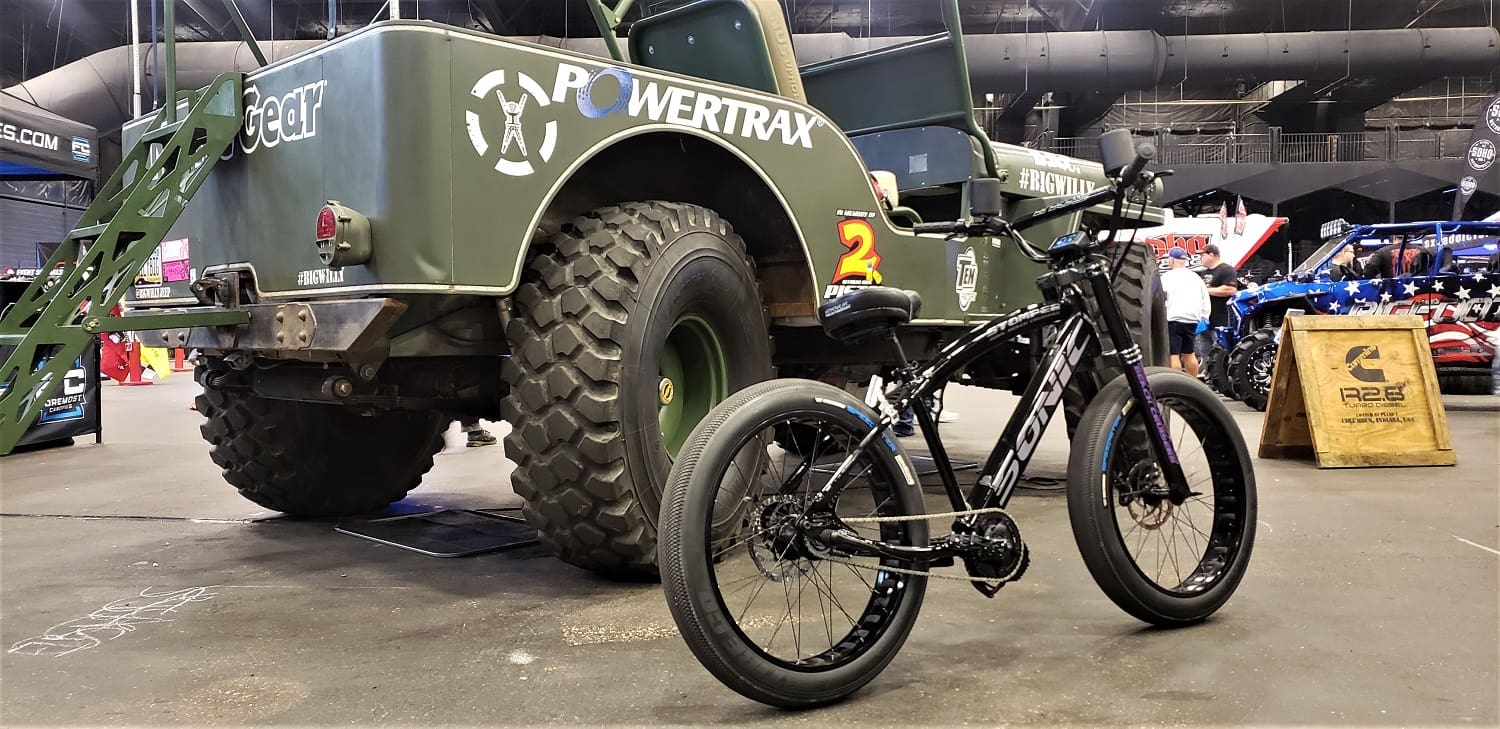 Military truck and bicycle displayed indoors.