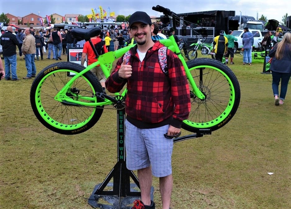 Man posing with green bicycle at event.