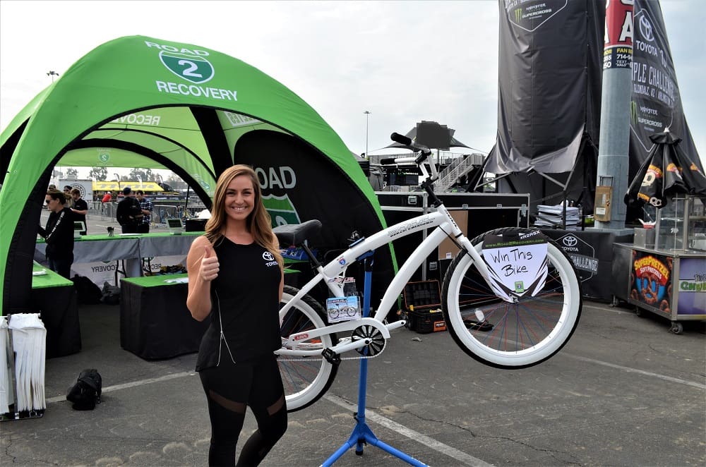 Woman smiling beside bicycle giveaway display tent.