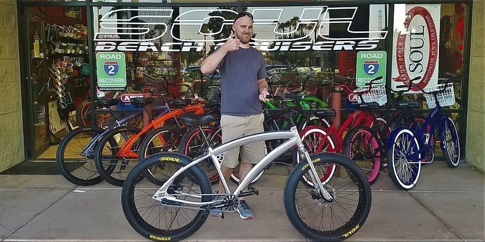Man standing with a bicycle outside shop.