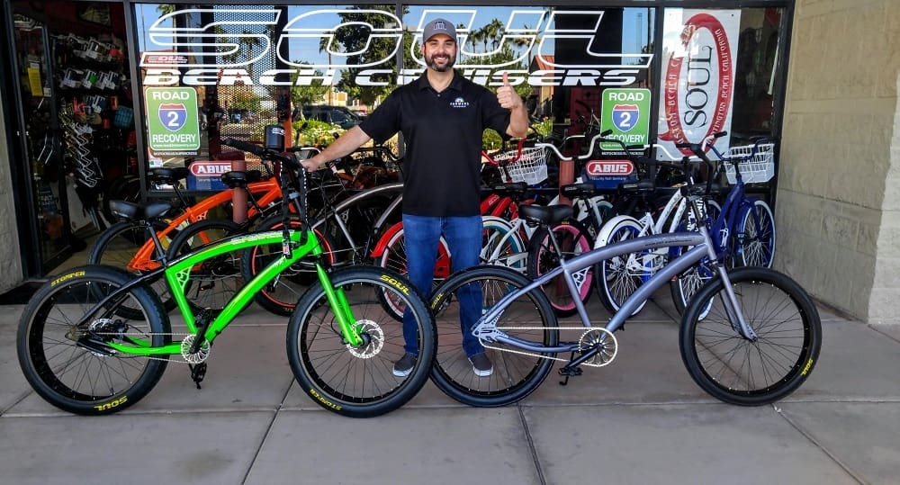 Man standing with two colorful bicycles outside.