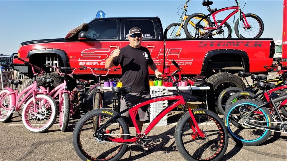 Man posing with bicycles at outdoor event.