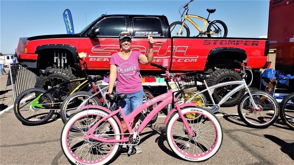 Woman posing with pink bicycle, truck background.