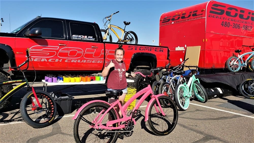 Girl posing with pink bicycle at event.