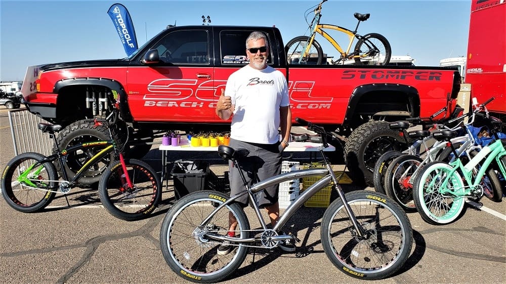 Man posing with bicycles at outdoor event.