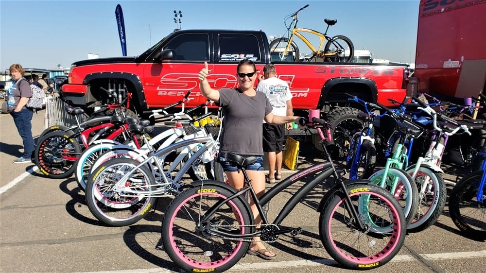 Woman posing with custom bicycles at event.