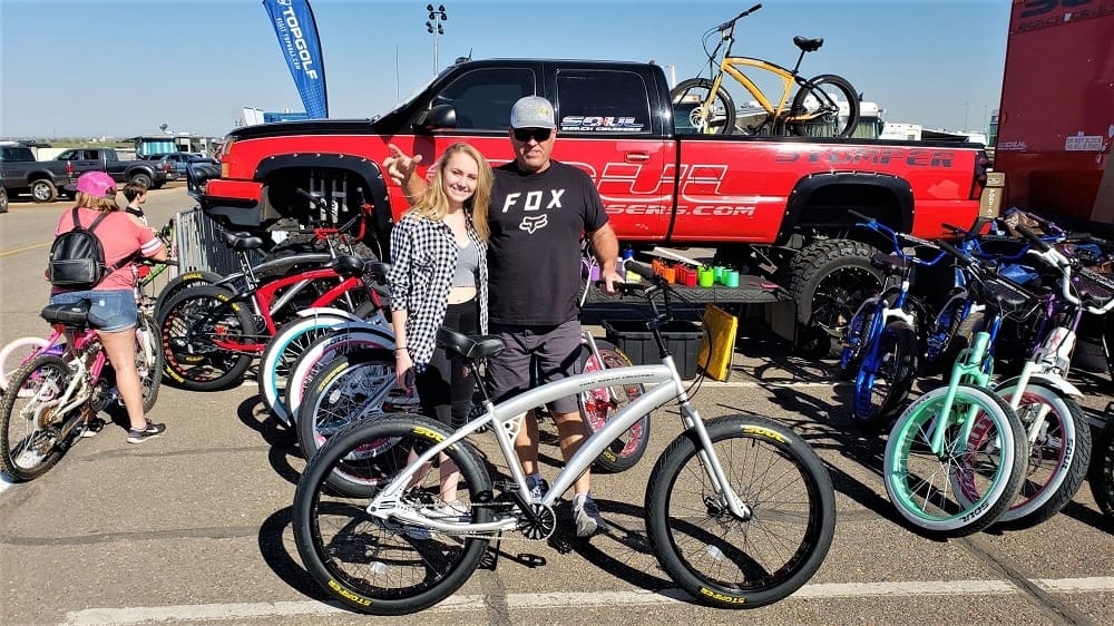 People posing with bikes at outdoor event.