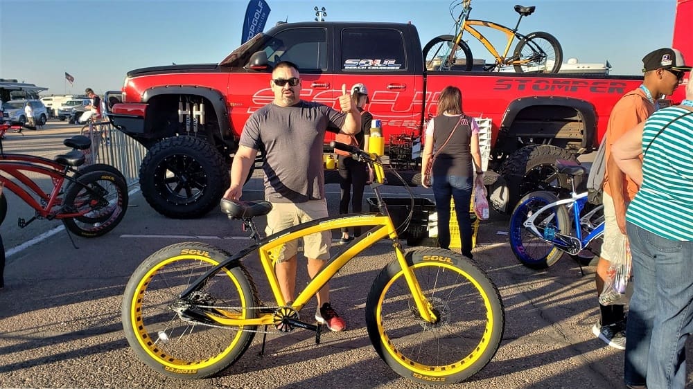 Man holding yellow bike at outdoor event.