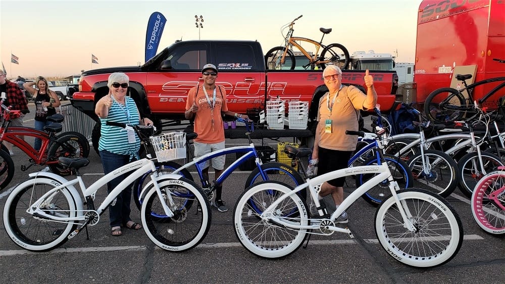 People posing with bicycles at outdoor event.
