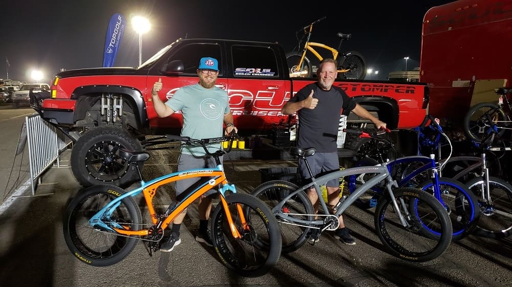 Two men with bicycles at night event.