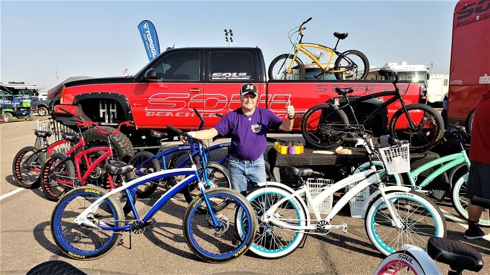 Man showcasing colorful bicycles in front of truck.