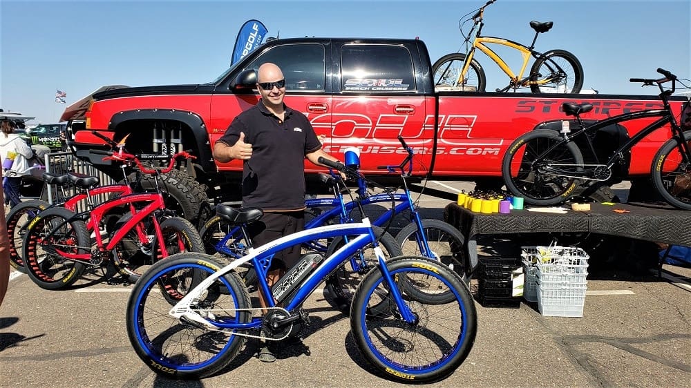 Man posing with bicycles at outdoor event.