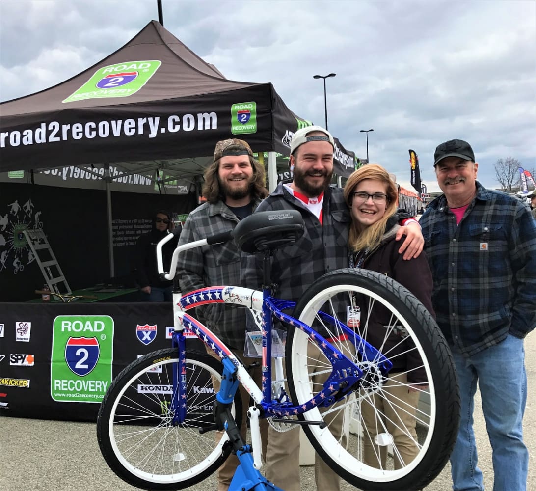Group posing with bike at event tent.