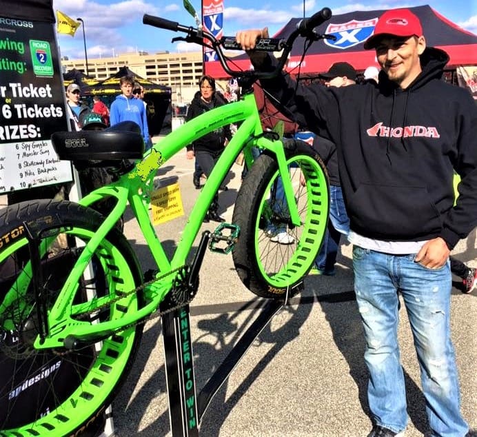 Man posing with bright green bicycle outdoors.
