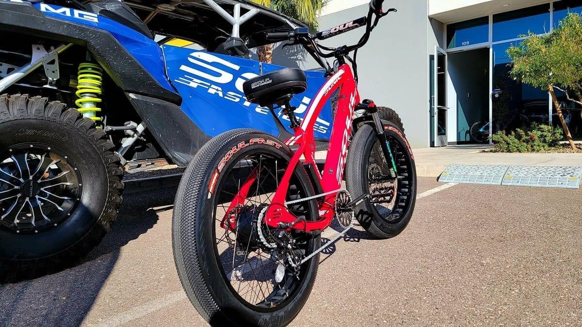 Red electric bike parked beside blue vehicle.