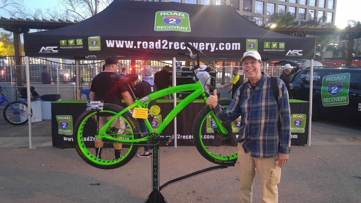 Man posing with green bicycle at event.