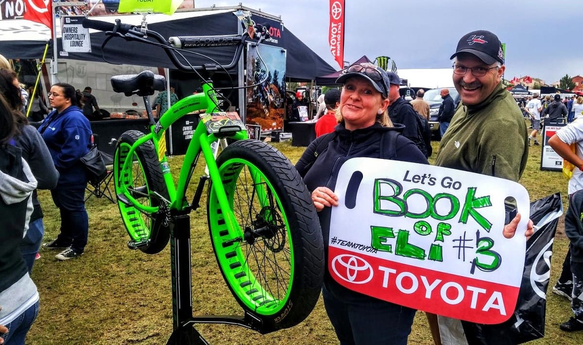 People posing with green bike and sign.