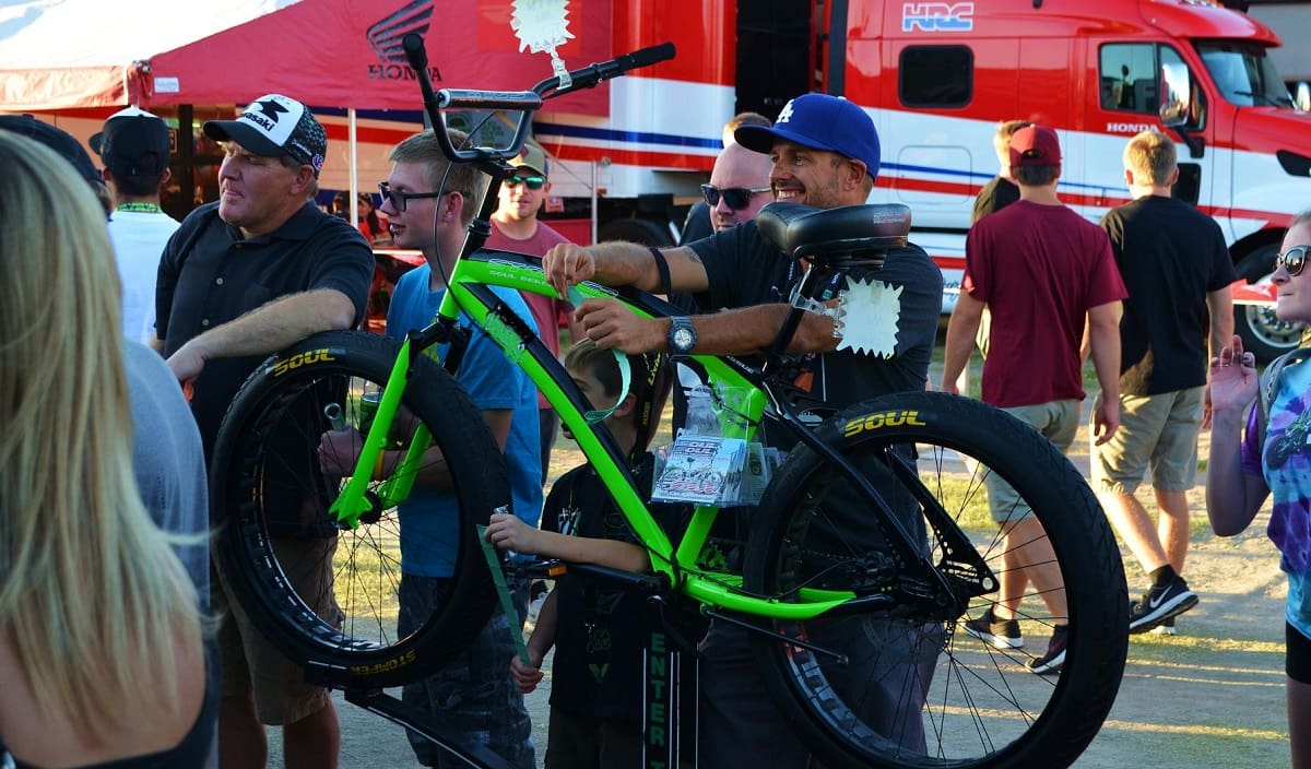 Man holding green bike at outdoor event.