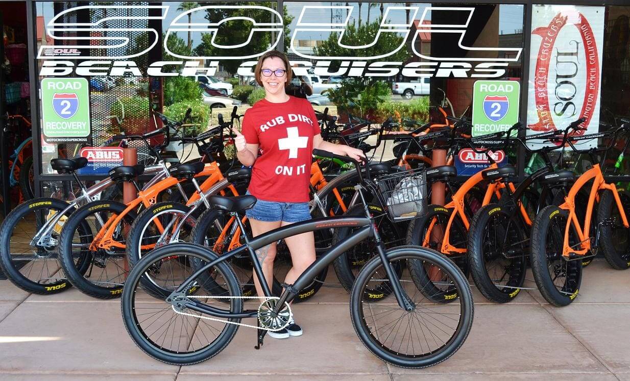 Person posing with black bicycle outside shop.