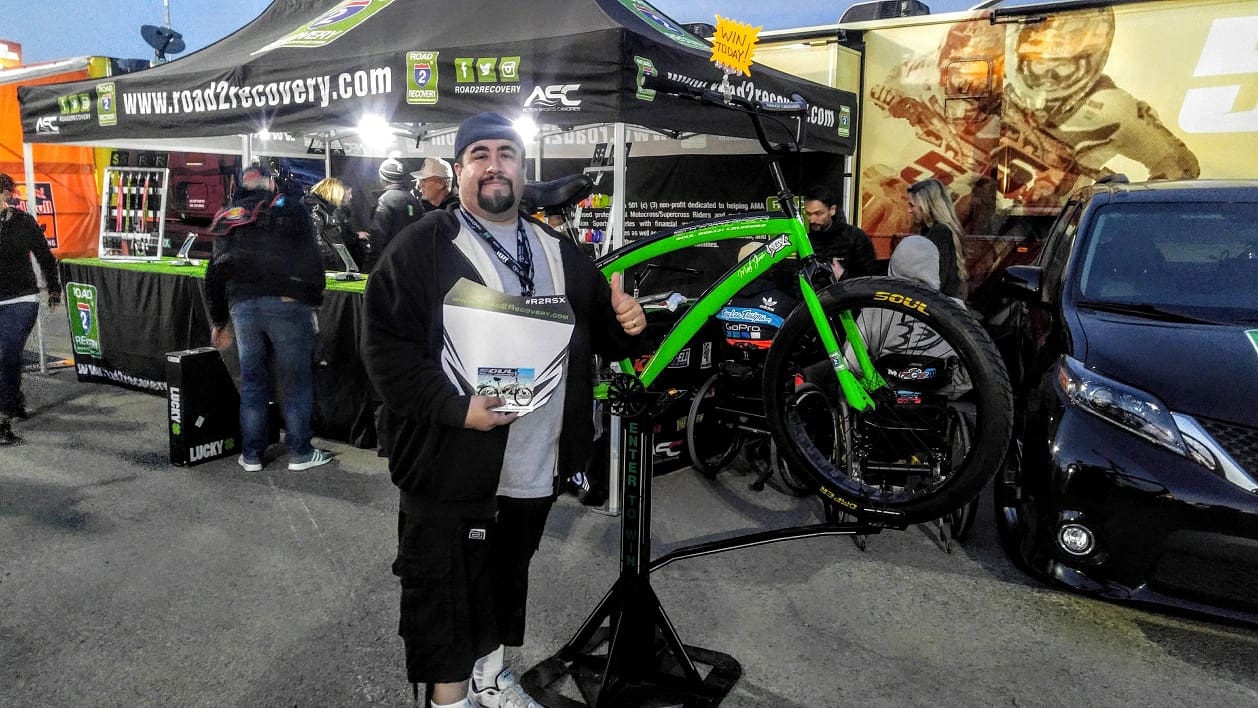 Man standing with bicycle at outdoor event.