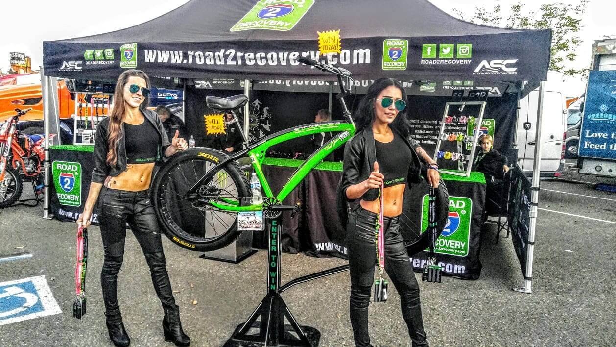 Women posing with bike at event booth.