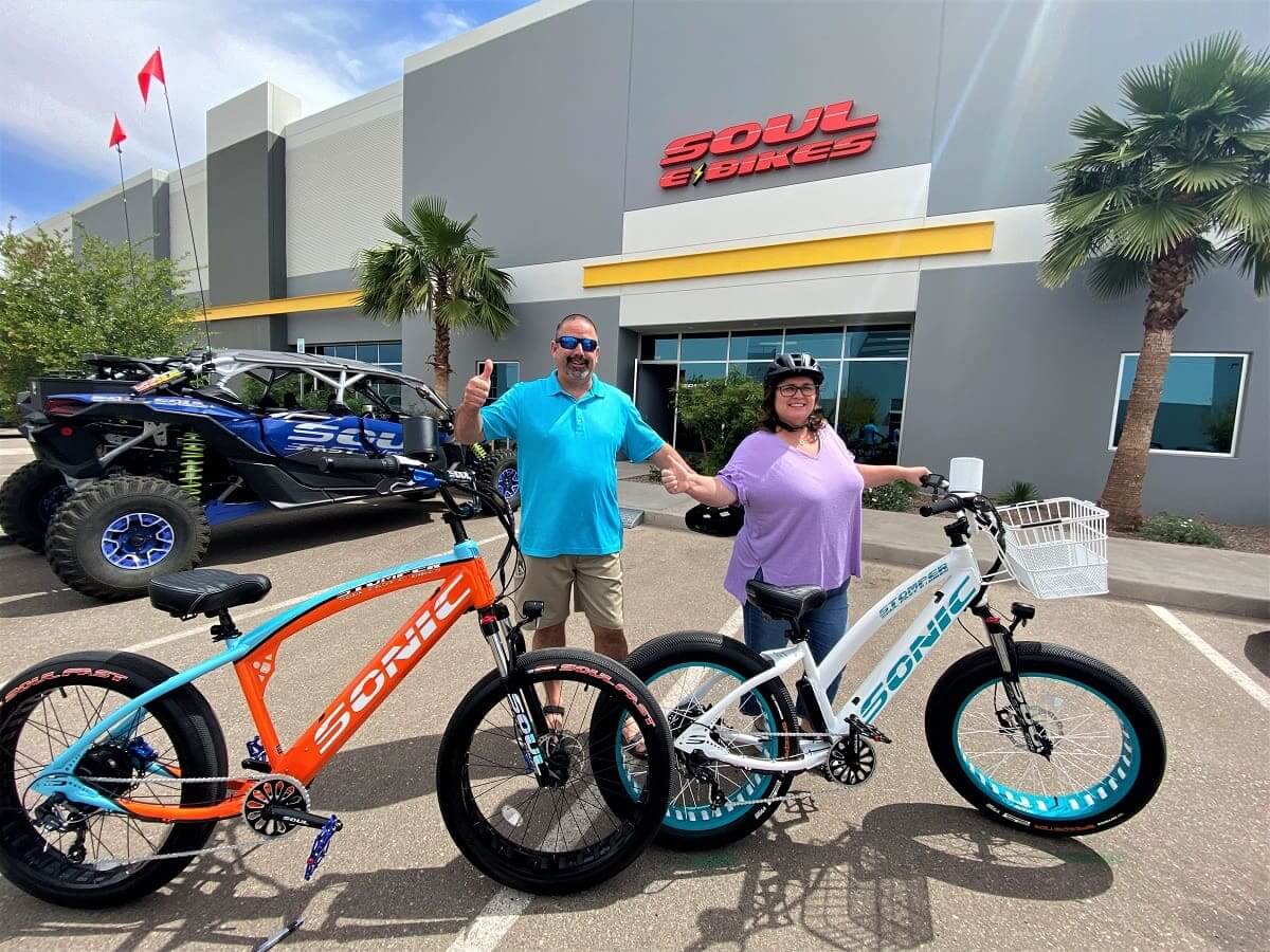 Two people with electric bikes outside store.