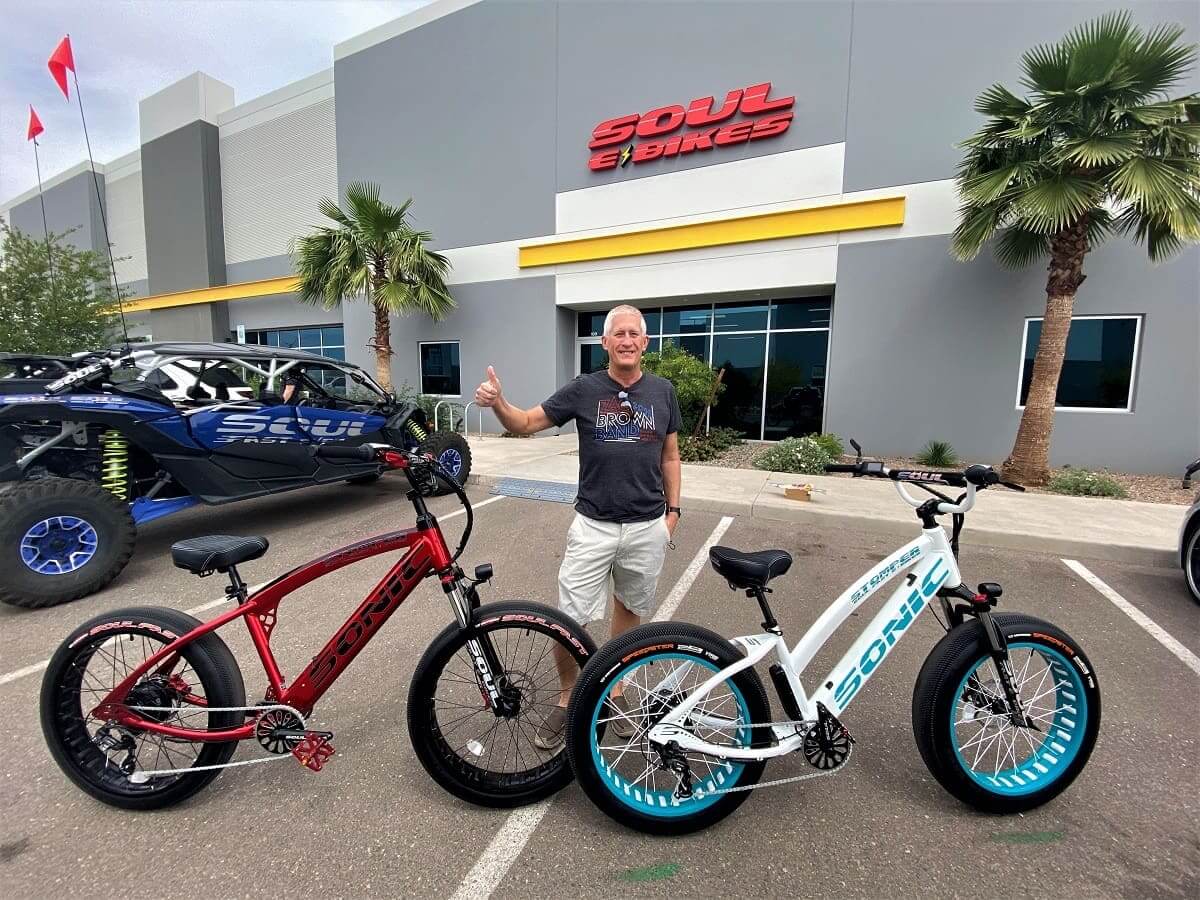 Man with two electric bikes outside store.